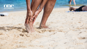 Image of person on a beach holding their foot due to what appears to be outside foot pain