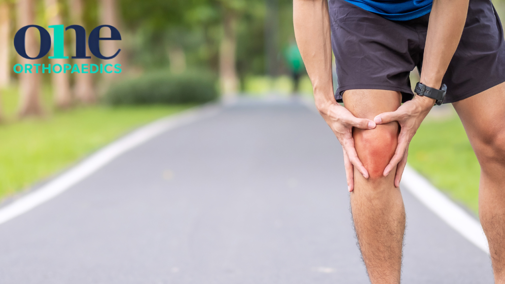 Person stopped on a path holding their knee which looks to be in pain